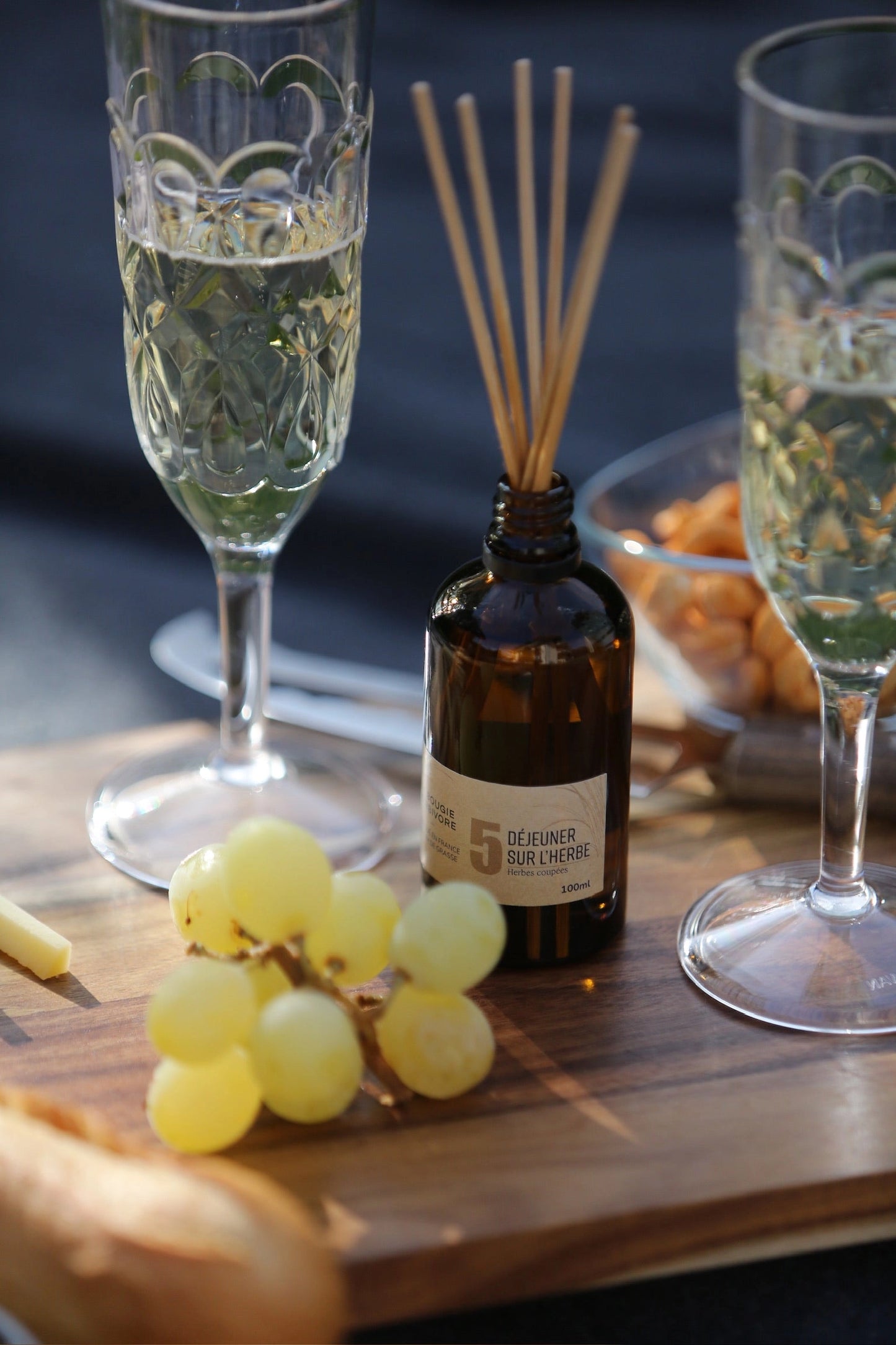 Diffuseur naturel made in France en verre avec tiges à arômes, accompagné de raisins et de coupes de champagne