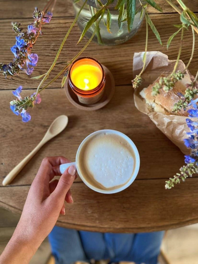 Bougie parfumée cèdre bergamote allumée sur une table en bois avec une tasse de café et des fleurs