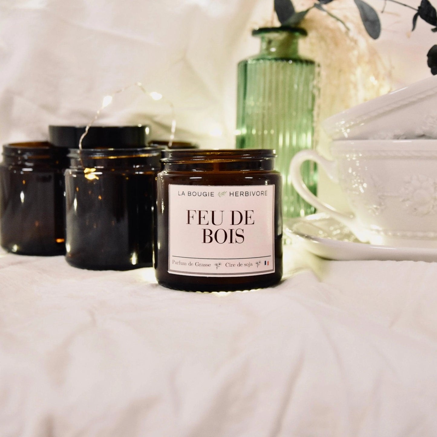 Bougie parfumée feu de bois de La Bougie Herbivore avec un pot en verre brun sur un fond doux