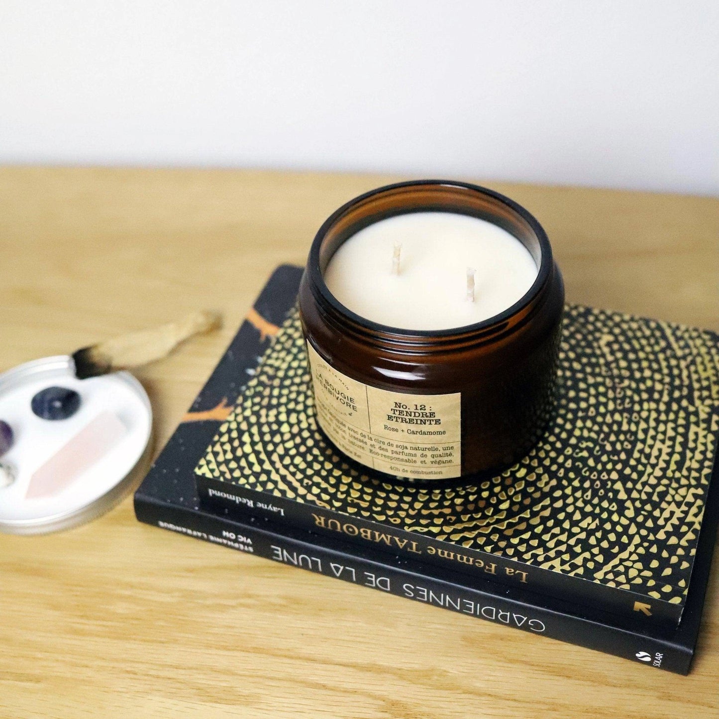 Bougie rose cardamome de La Bougie Herbivore en pot en verre sur une table avec des livres